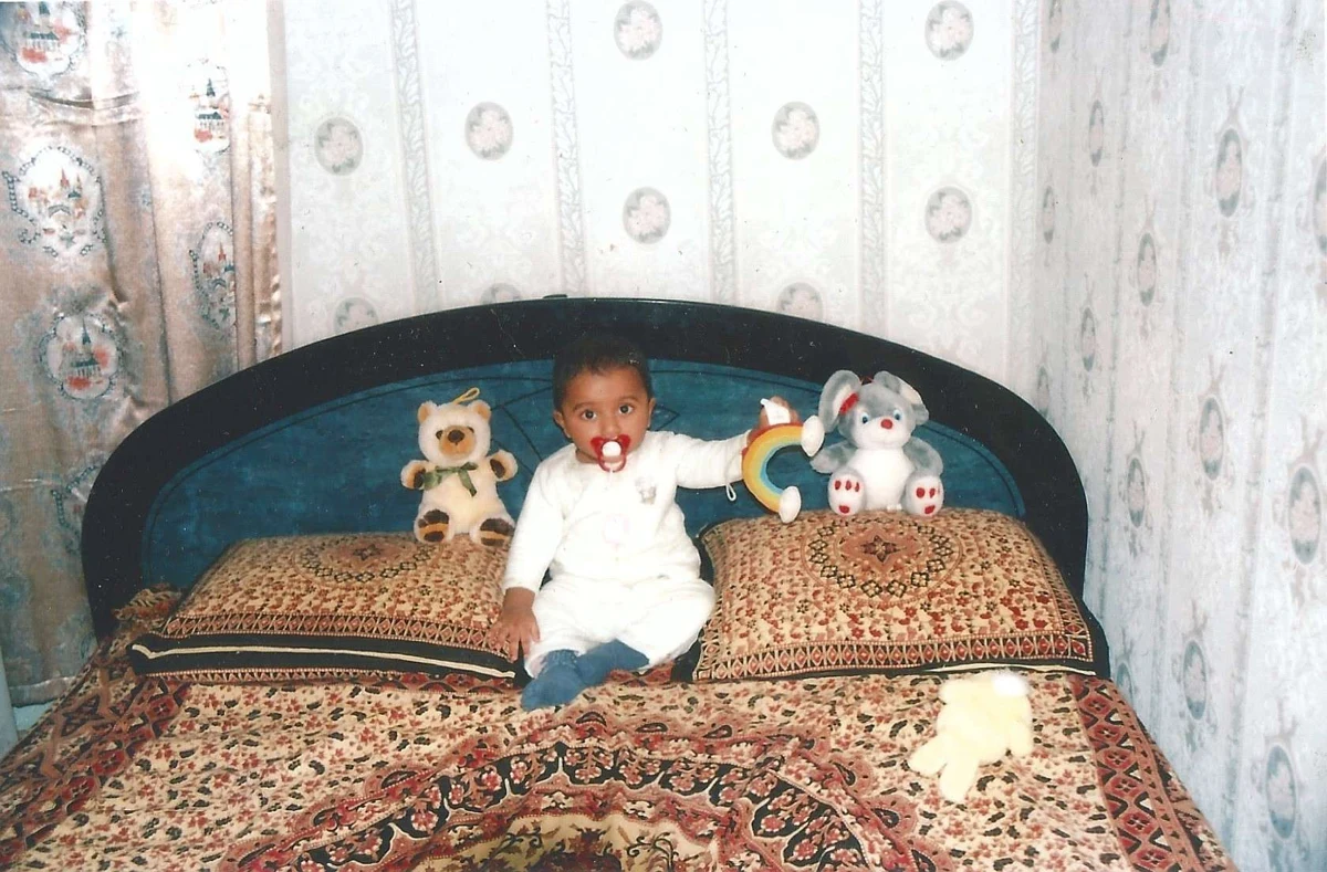 Lasry bébé, assis entre ses peluches sur un lit aux motifs colorés.