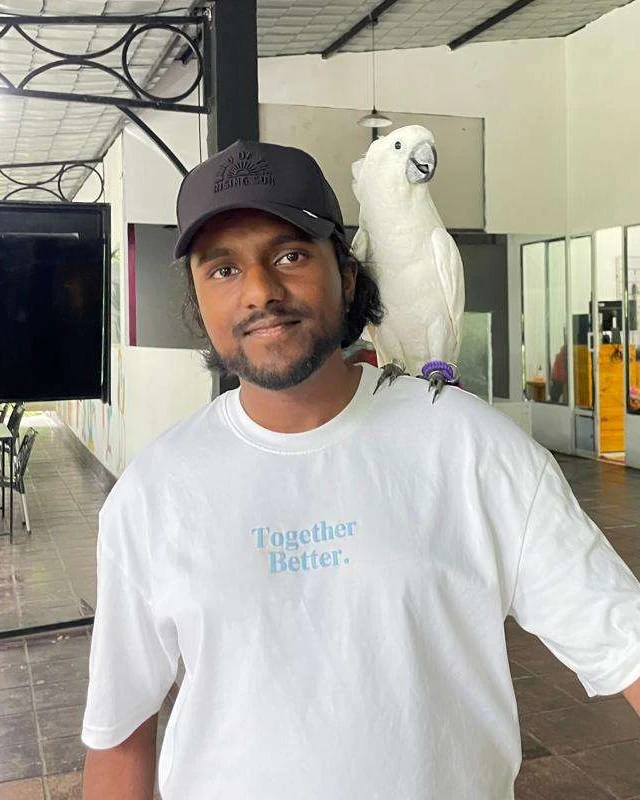 Lasry BESKIWIN, en casquette noire et tee-shirt blanc, avec un perroquet blanc sur l’épaule.